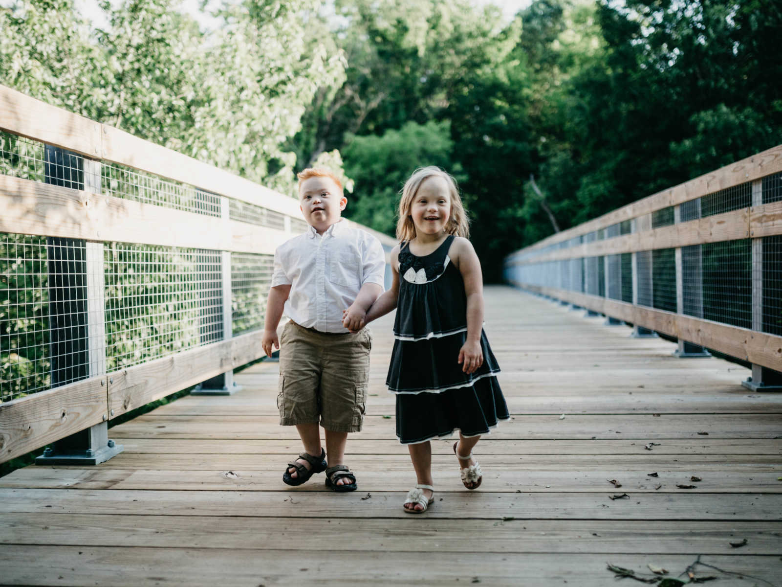 Down syndrome boy and girl hand in hand walking across bridge