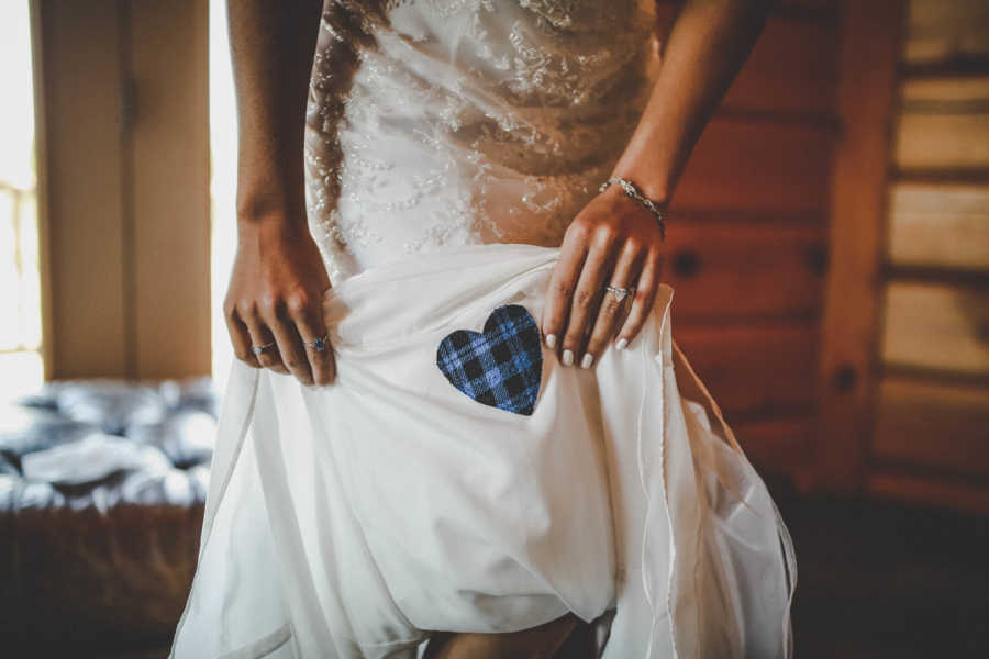 Bride holds up skirt of dress that has heart sewed on made out father's flannel shirt