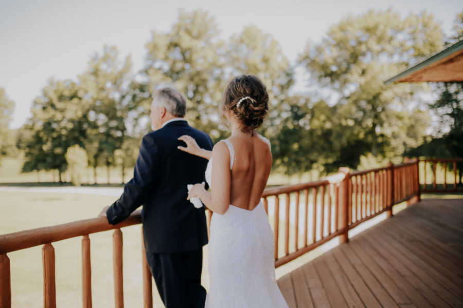 Daughter in wedding gown taps shoulder of farmer father 