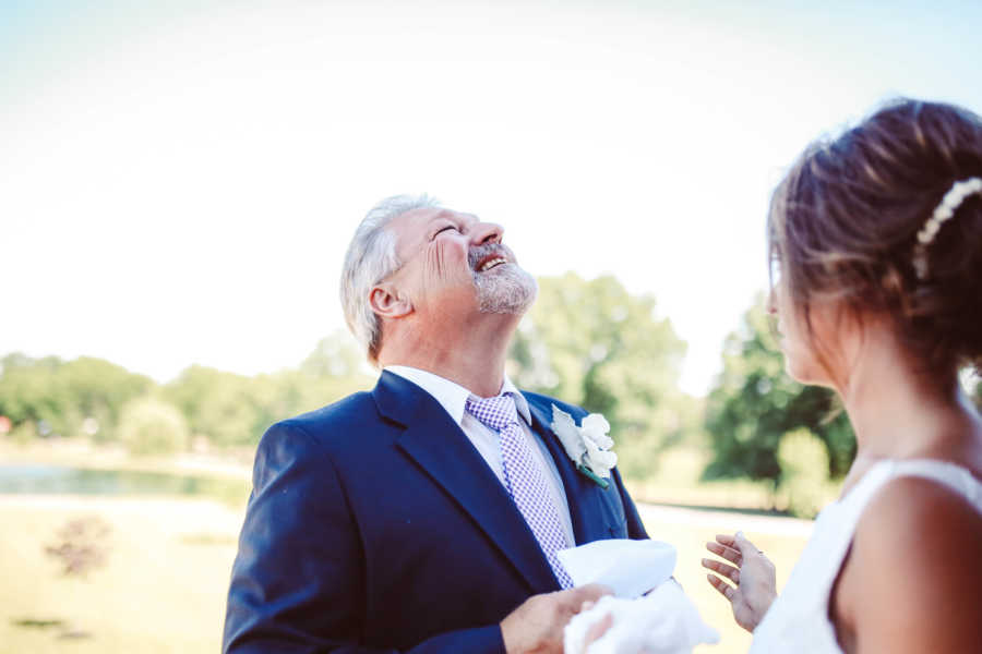 Father of bride looks up smiling next to daughter in wedding gown