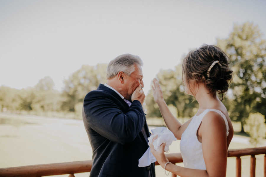 Farmer father holds hand to mouth crying from seeing daughter in bridal gown