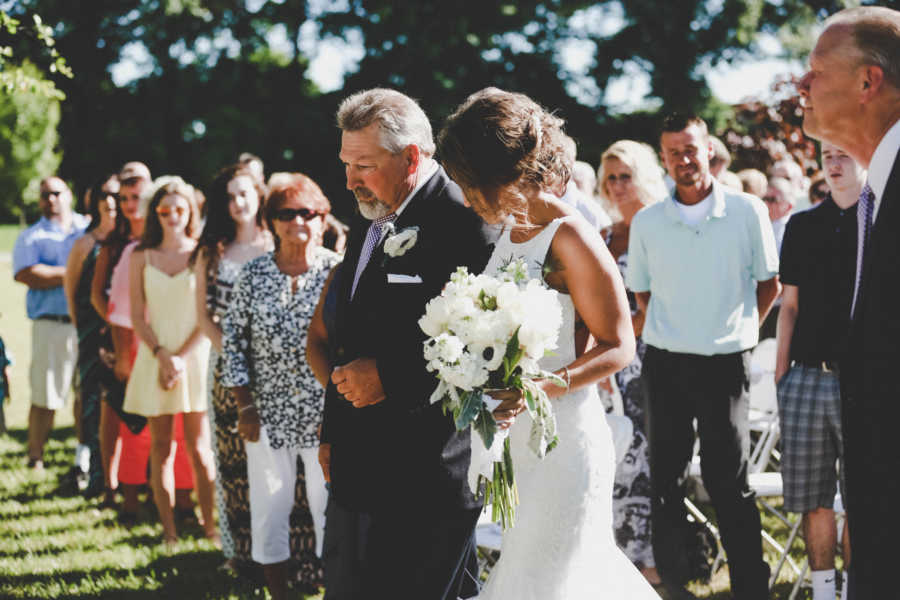Father walks daughter down aisle at wedding with guests watching