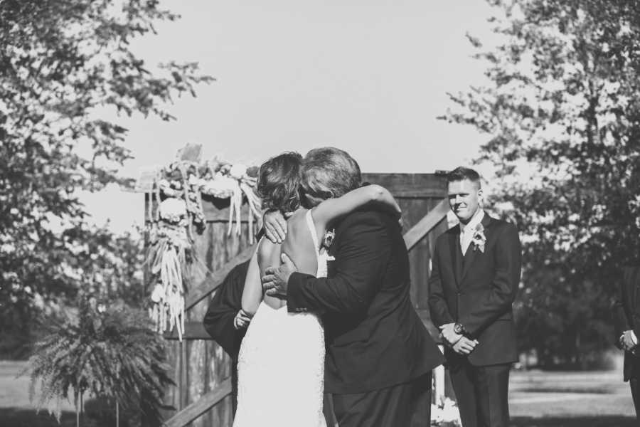 Father hugs and kisses daughter on the cheek as he gives her away at the altar