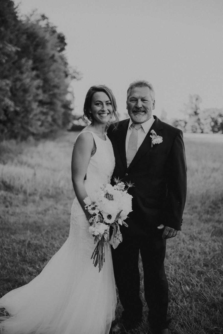 Bride and father stand arm in arm in field at wedding