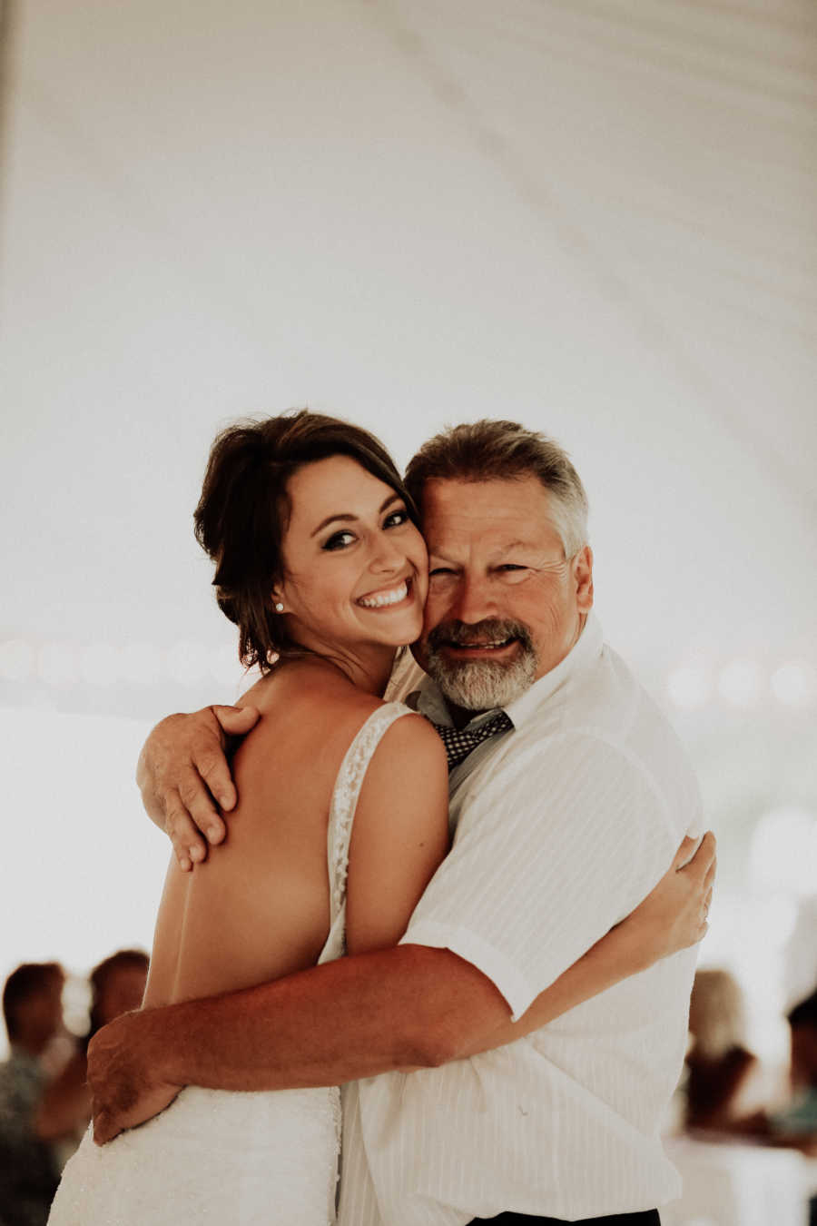 Father and bride smile while hugging at wedding reception