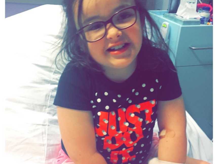 Little girl with glasses smiles in hospital bed