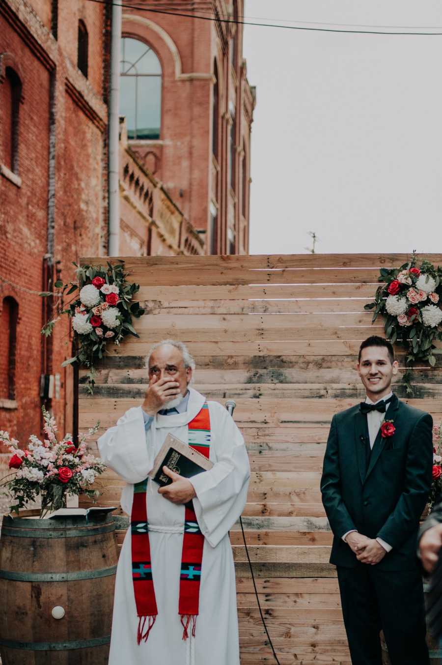 Groom smiles watching bride walk down the aisle while stepdad stands with hand over his mouth