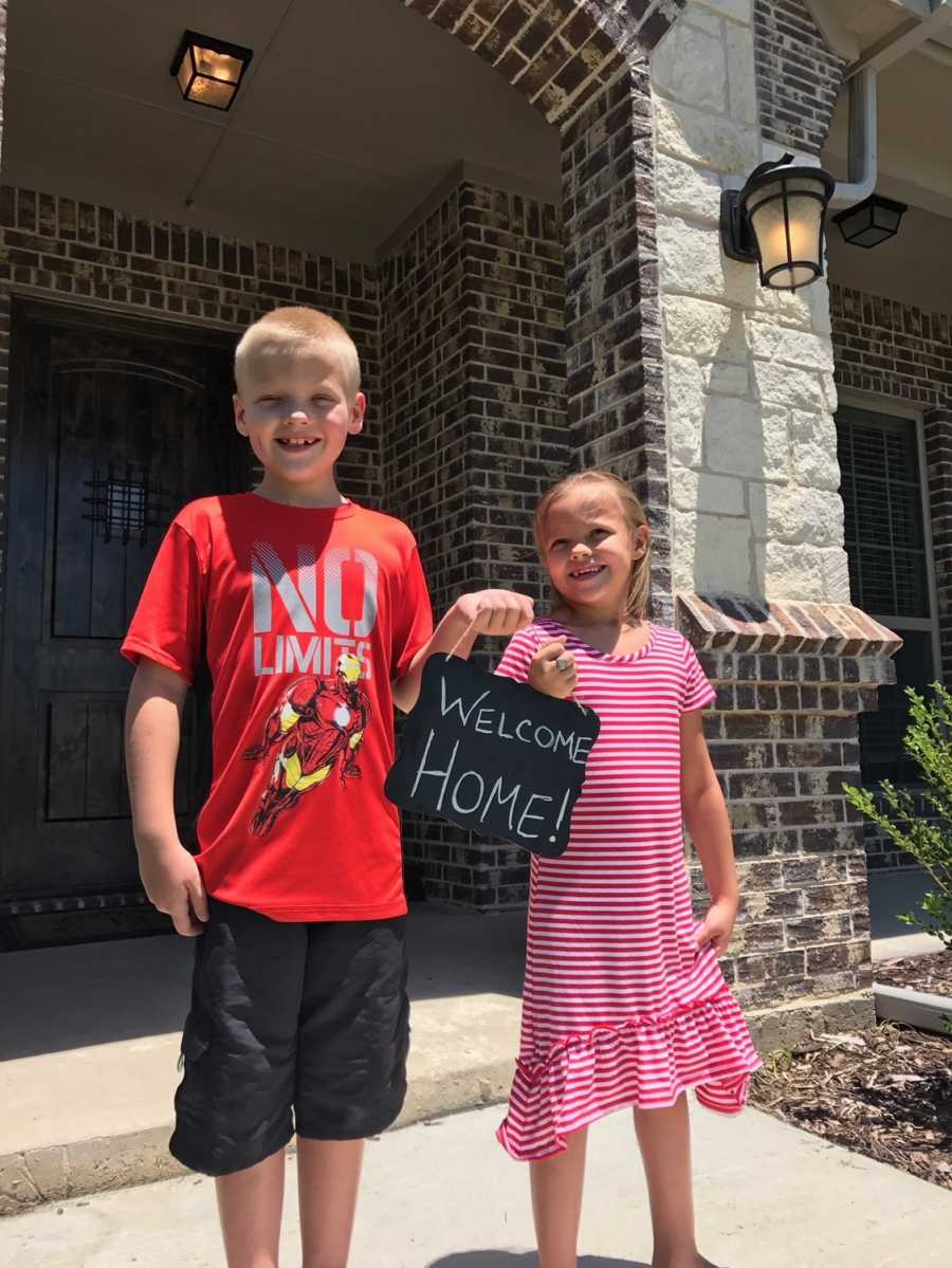 Birth son and daughter hold sign on front walkway of house saying, "Welcome home" for adopted sibling