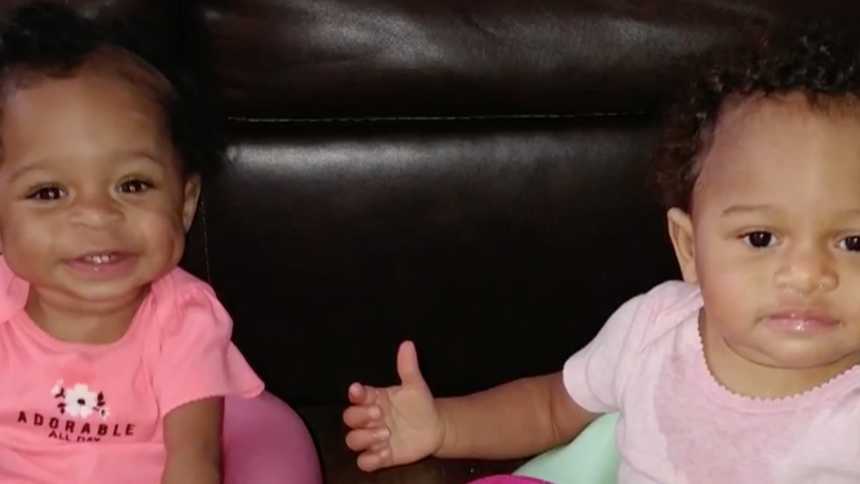 Adopted infant twins who were once abused sit next to each other smiling