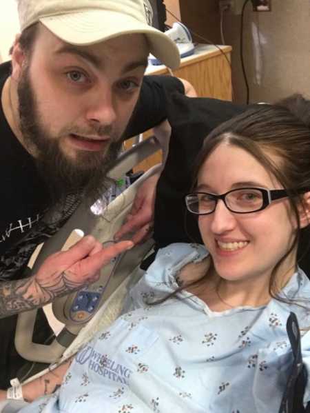 Sober pregnant woman lies in hospital bed with husband leaning over 