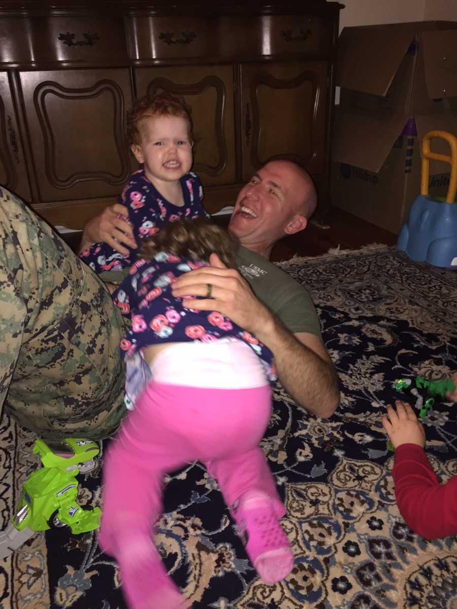 Toddler who needs open heart surgery sits on chest of father who is lying on ground with sister