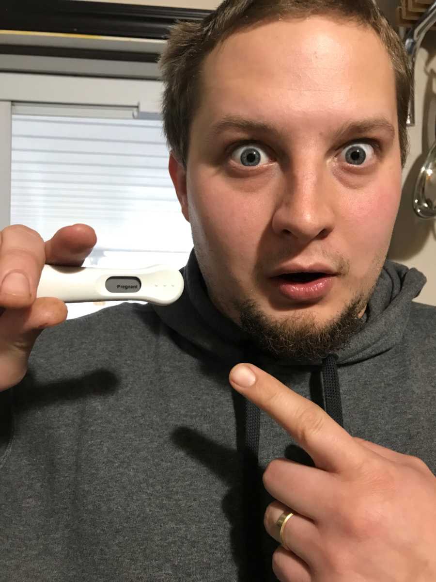 Husband pointing to pregnancy test that says, "pregnant" with shocked look on his face