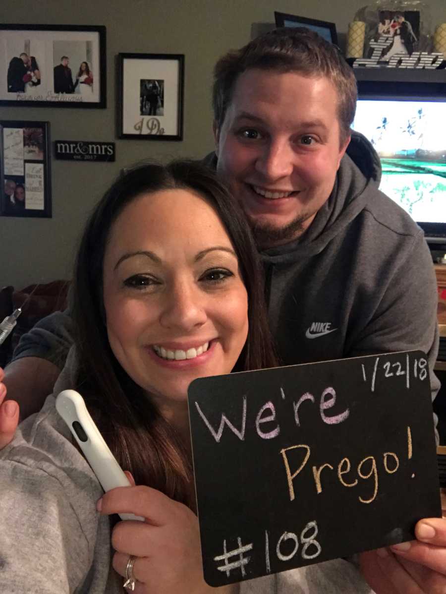 Wife who struggled with infertility hold pregnancy test while husband holds sign saying, "we're prego"