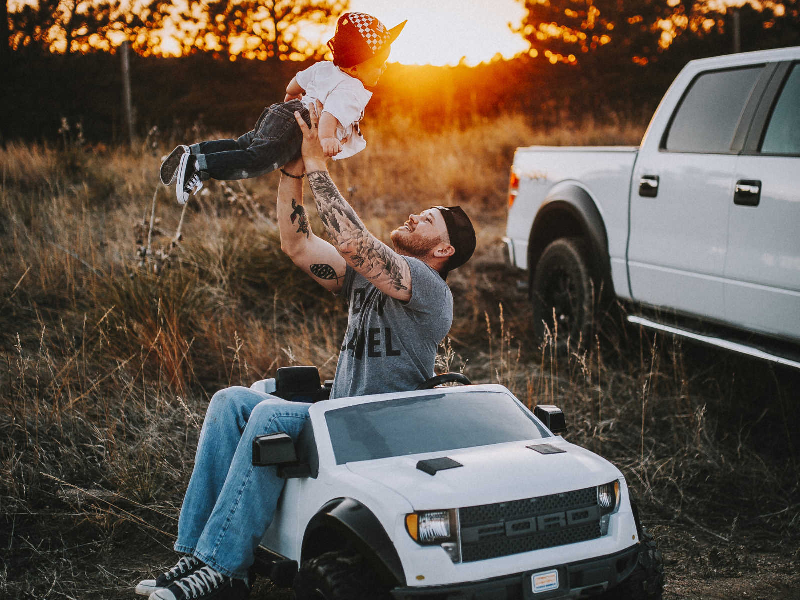 Father sits in toy truck throwing his son in the sir with his real truck in the background