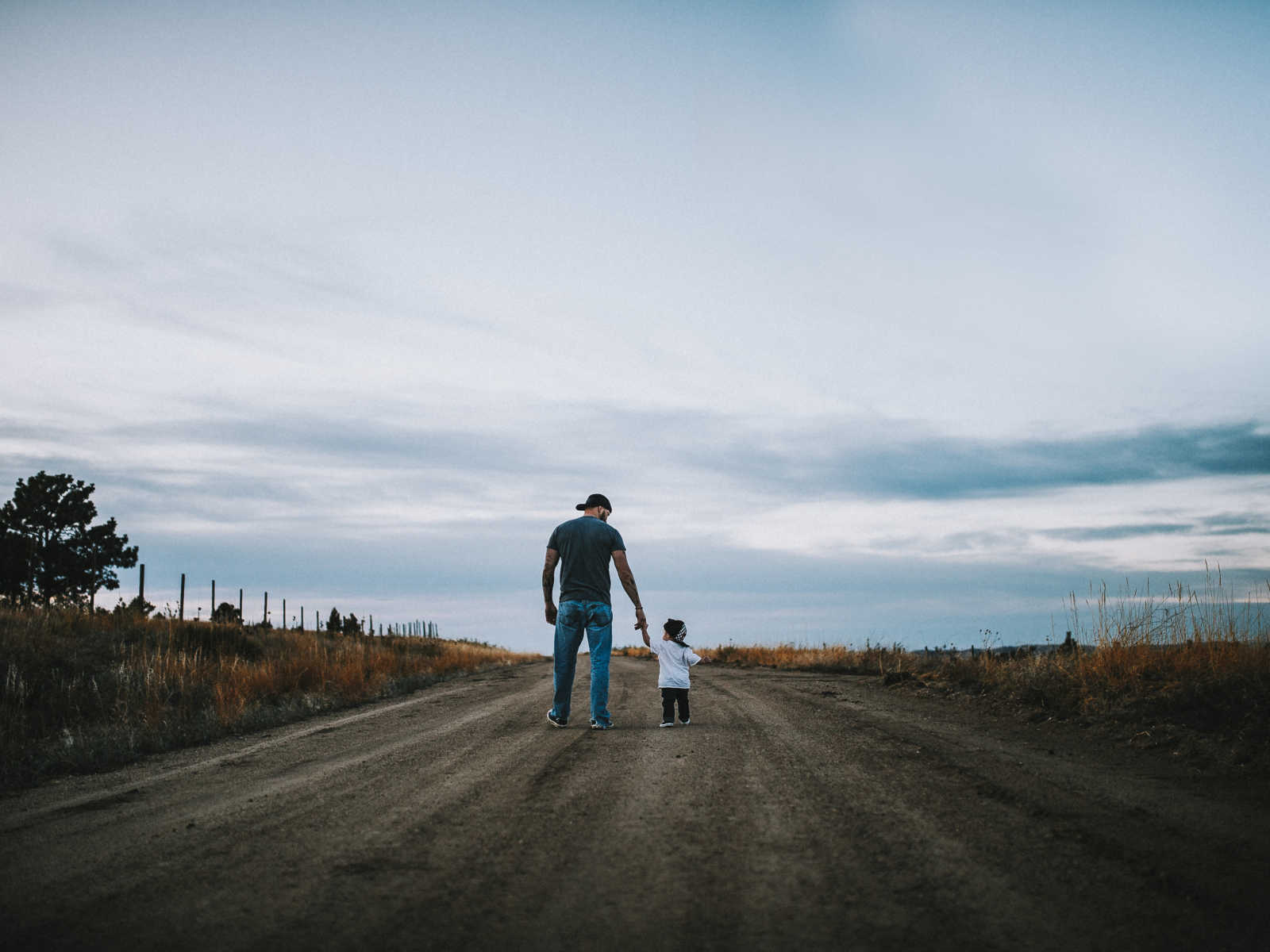 View from the back of father holding hands with his toddler son on dirt road