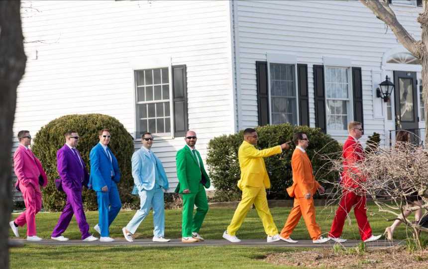 Men in colorful suits walk in line on sidewalk