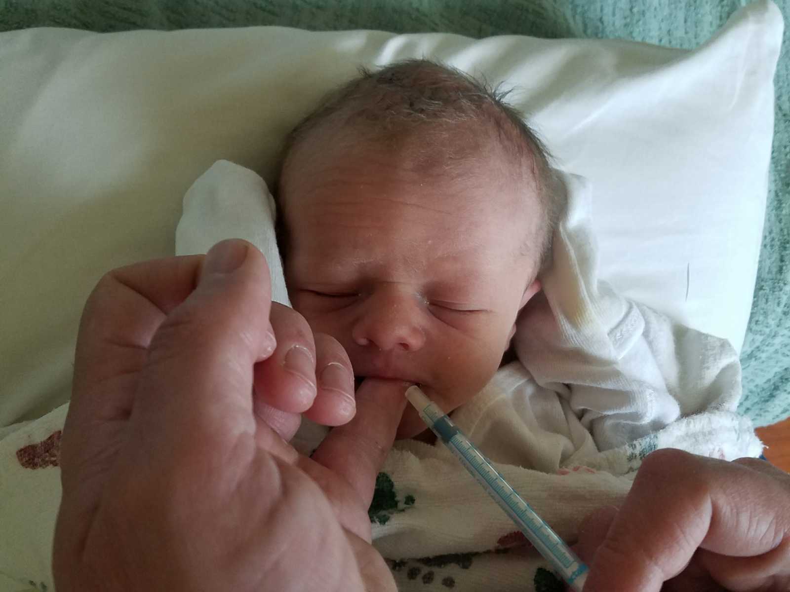 Close up of newborn whose mouth is being opened by an adult hand and a syringe is close to his mouth
