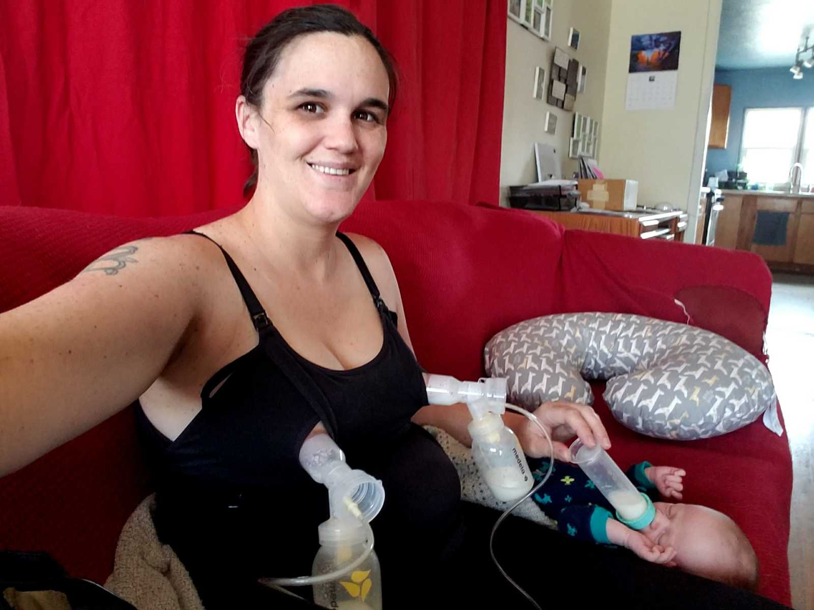 Woman takes selfie of her pumping milk while feeding her baby a bottle who is lying next to her on couch