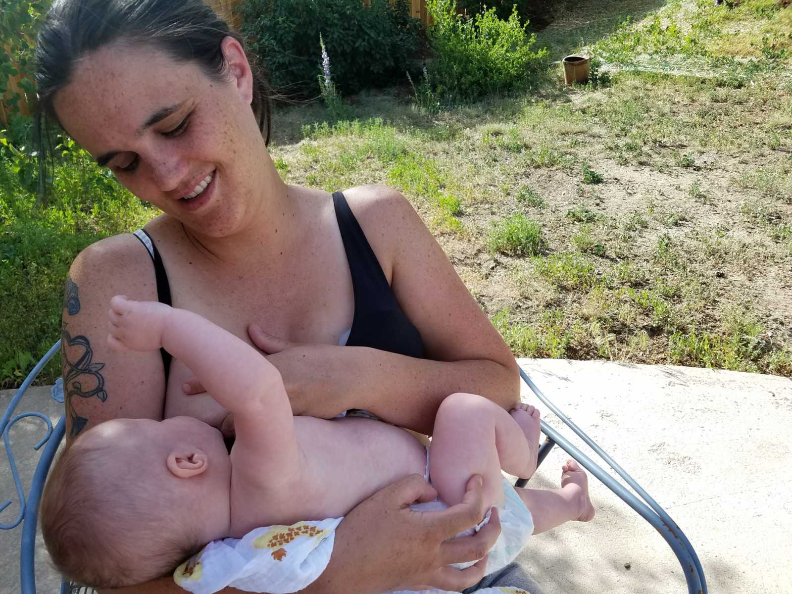 Woman looks down at baby smiling while baby breastfeeds