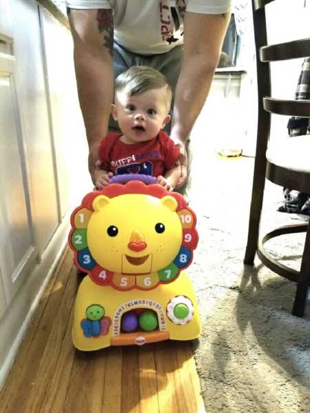 Baby with down syndrome being pushed by father while riding toy in house