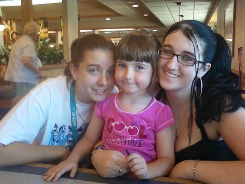 Teen mother with drug addiction sitting in booth with toddler daughter and friend