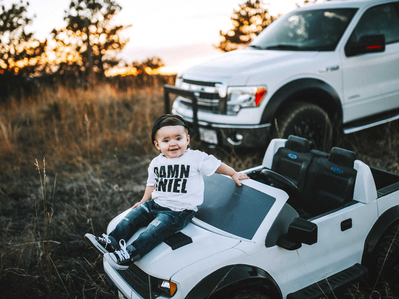 Toddler sits on hood of toy truck in front of father's real truck