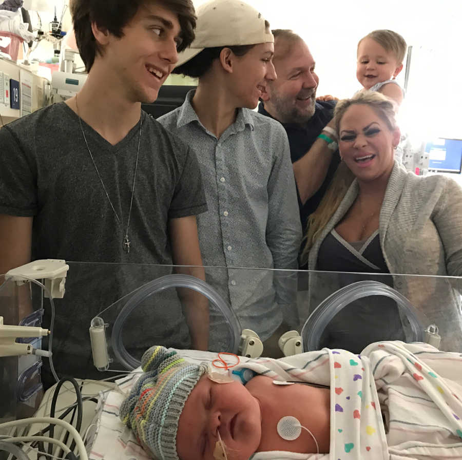 Woman who just gave birth stands over baby in NICU with infant son, older son, husband and husband's son