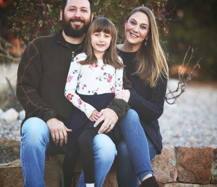 7 year old who received liver transplant sits on father's lap smiling next to mother