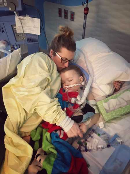 Mother lays in hospital bed with child who is sleeping with tubes attached to him 