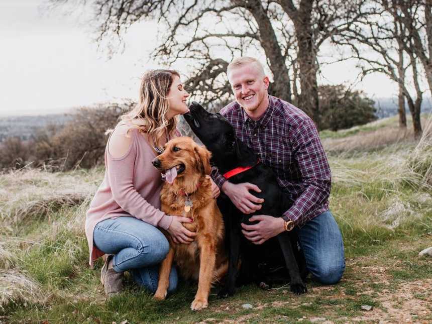 Daughter who wore deceased mother's wedding dress kneels with husband and two dogs in grass