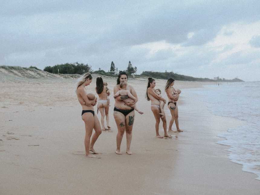 Topless woman breastfeeding on the beach near the shore