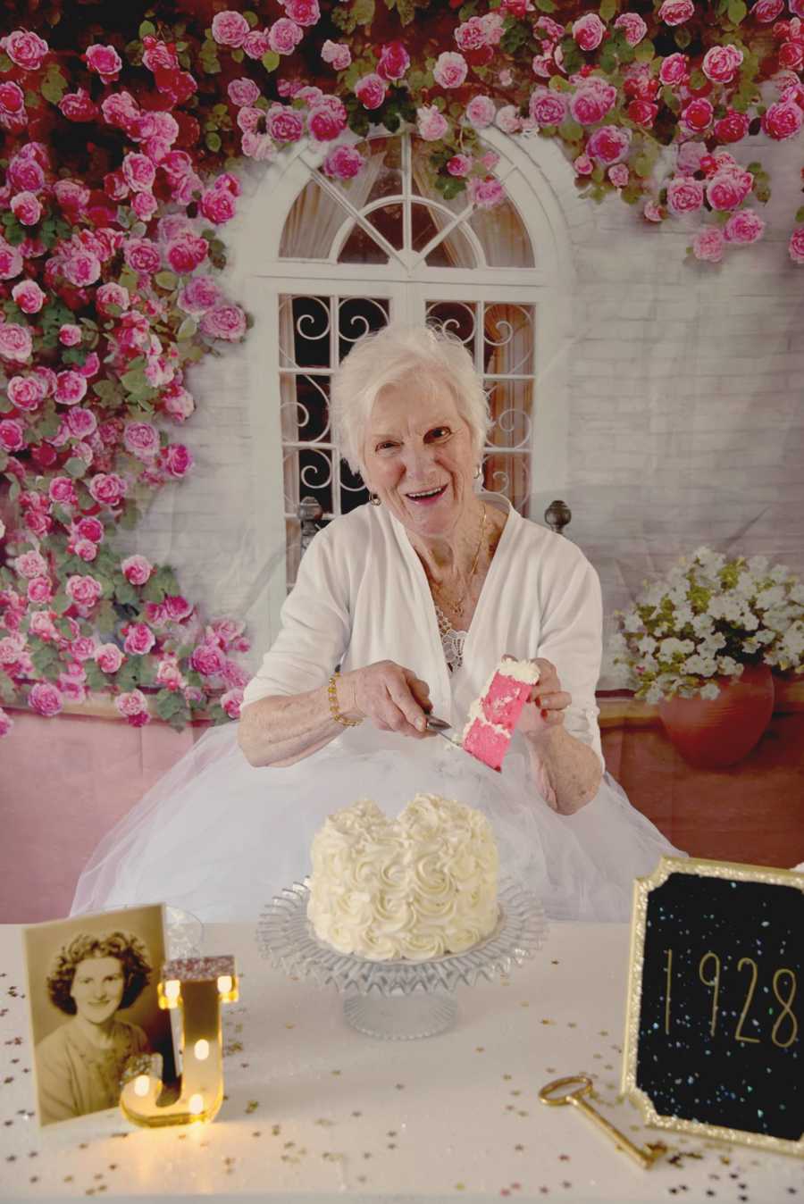 90 year old woman smiles while holding a piece of pink cake with white frosting in the air