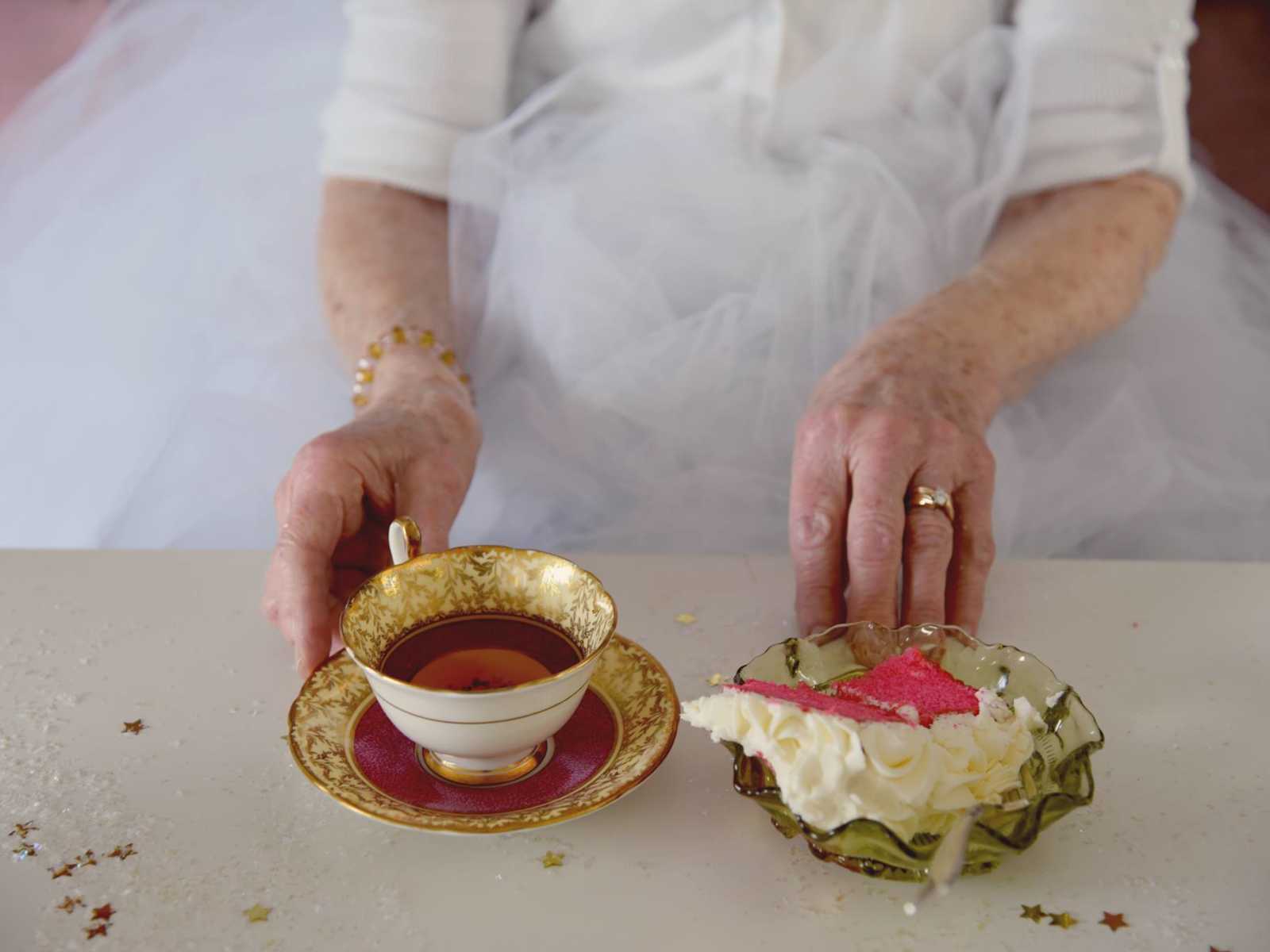 Close up of 90 year old woman's hand on plate of teacup and cake