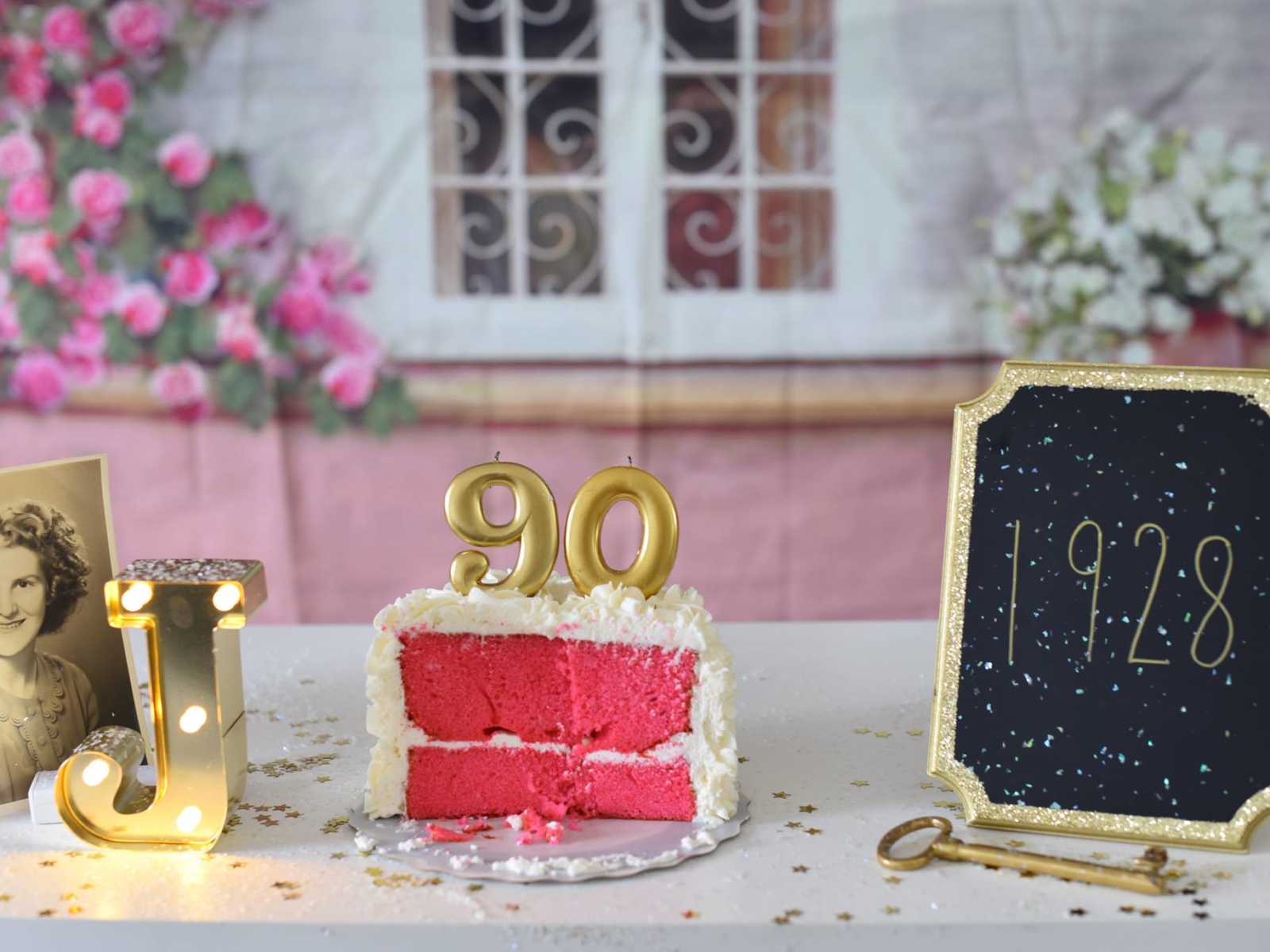 Table with pink cake with white frosting, letter J, whiteboard that says, 1928, and picture of 90th birthday girl 