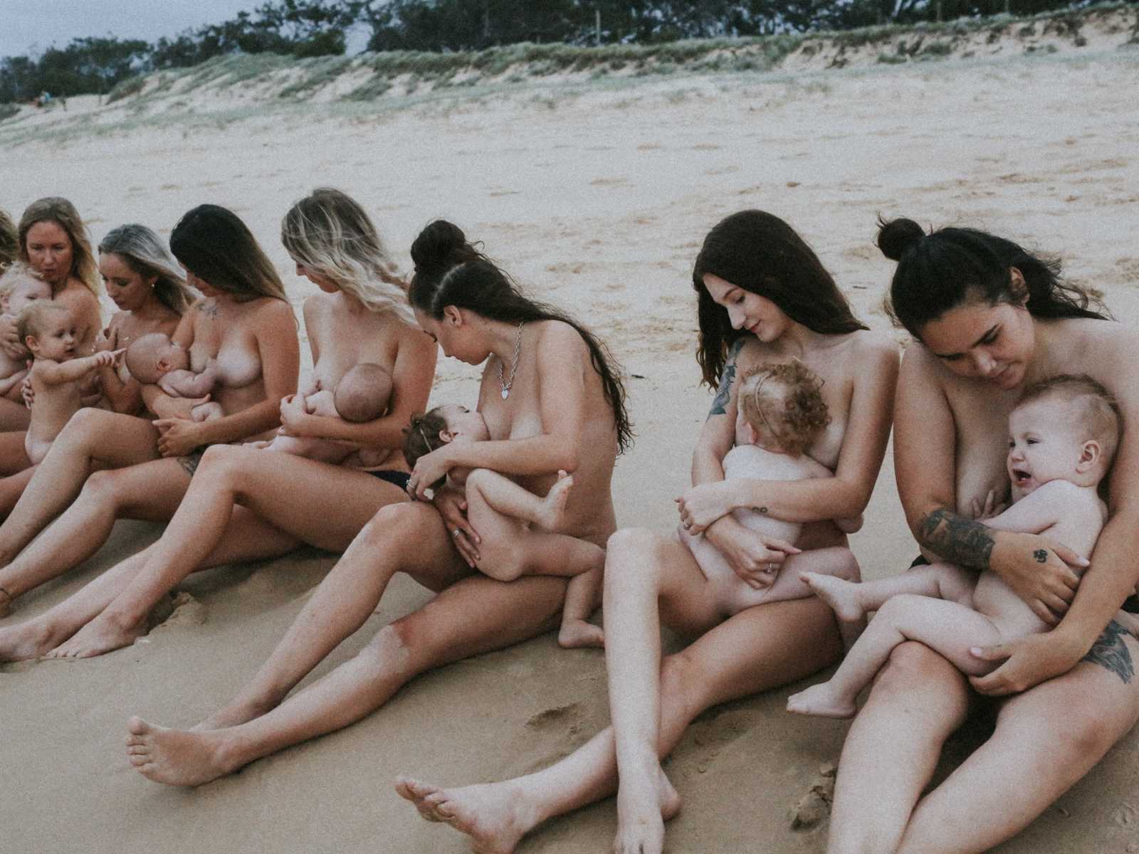 Row of naked woman sitting on the beach breastfeeding