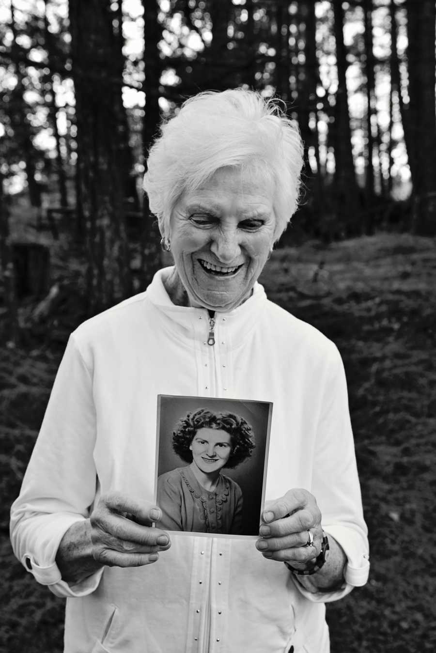 90 year old woman smiles down looking at picture of her younger self