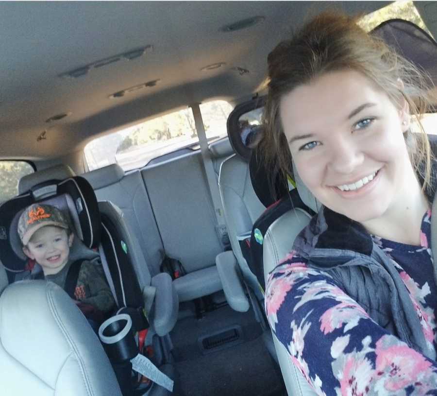 Woman who feels like bad mom takes selfie in car with toddler son in back in car seat 
