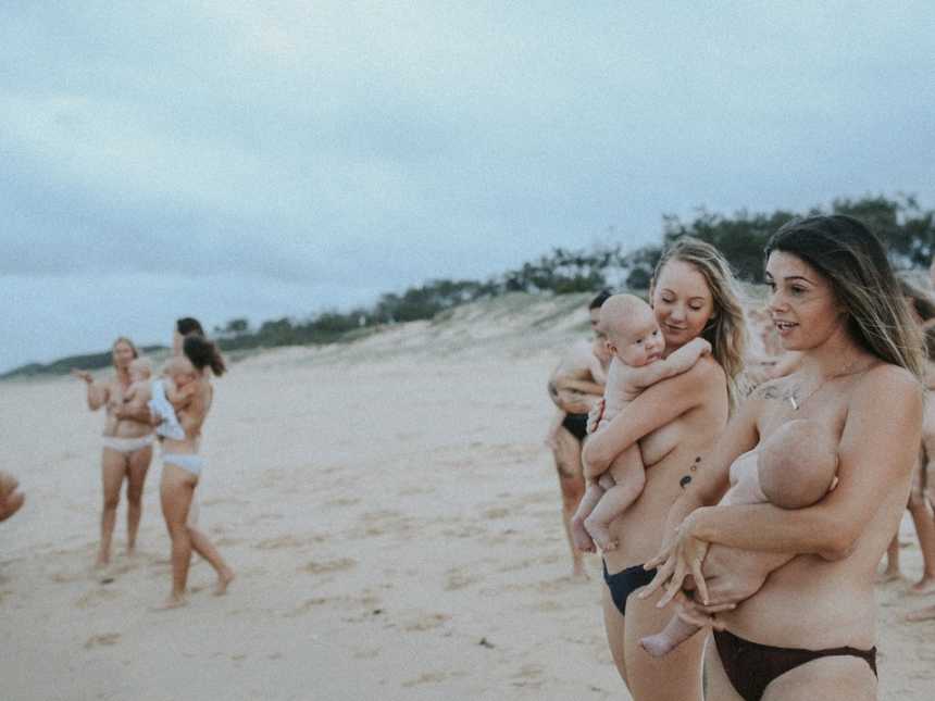 Topless woman stand and chat on the beach while breastfeeding