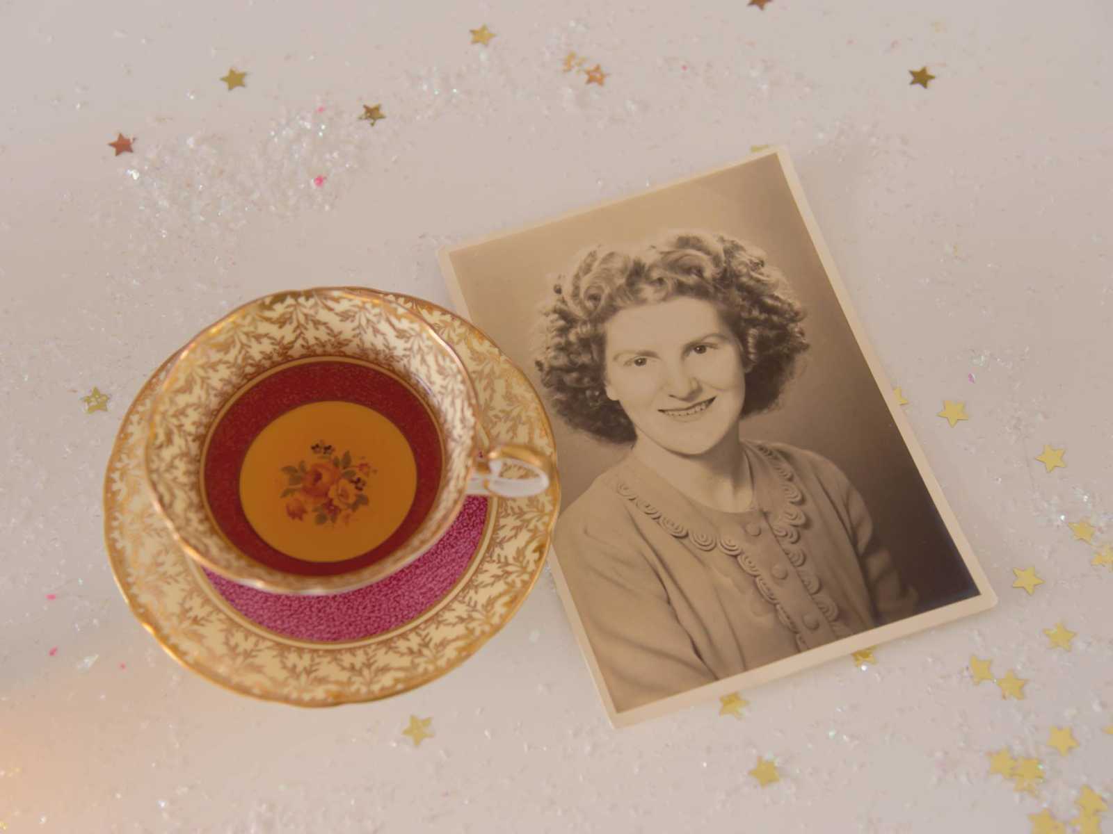 Tea cup sitting next to picture of 90 year old woman when she was younger