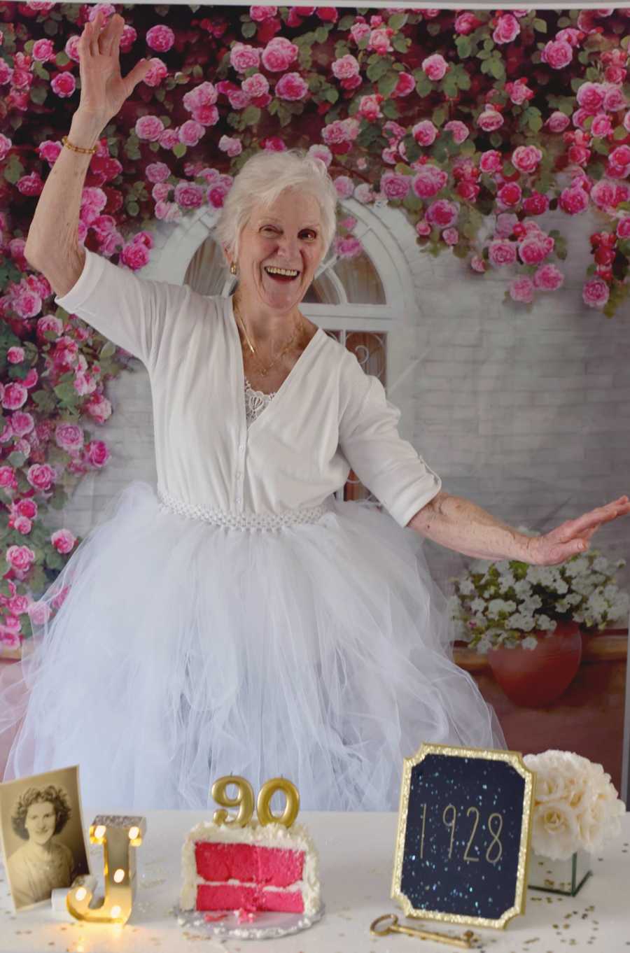 90 year old woman smiles while posing in front of birthday cake