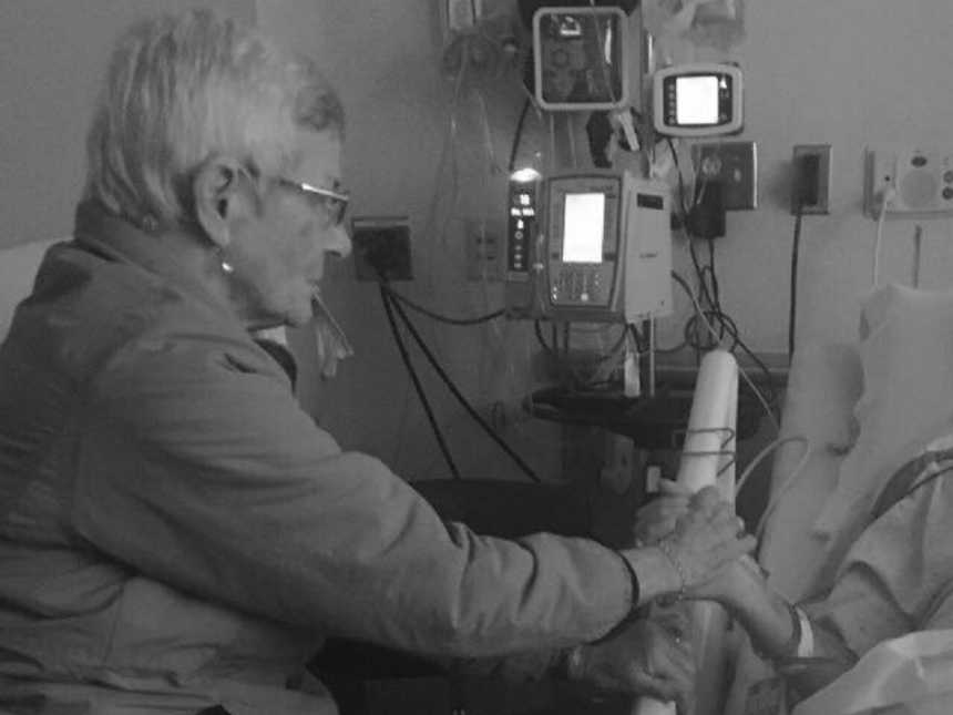 Mother with dementia sits on side of hospital bed hold hands with son who would soon pass away