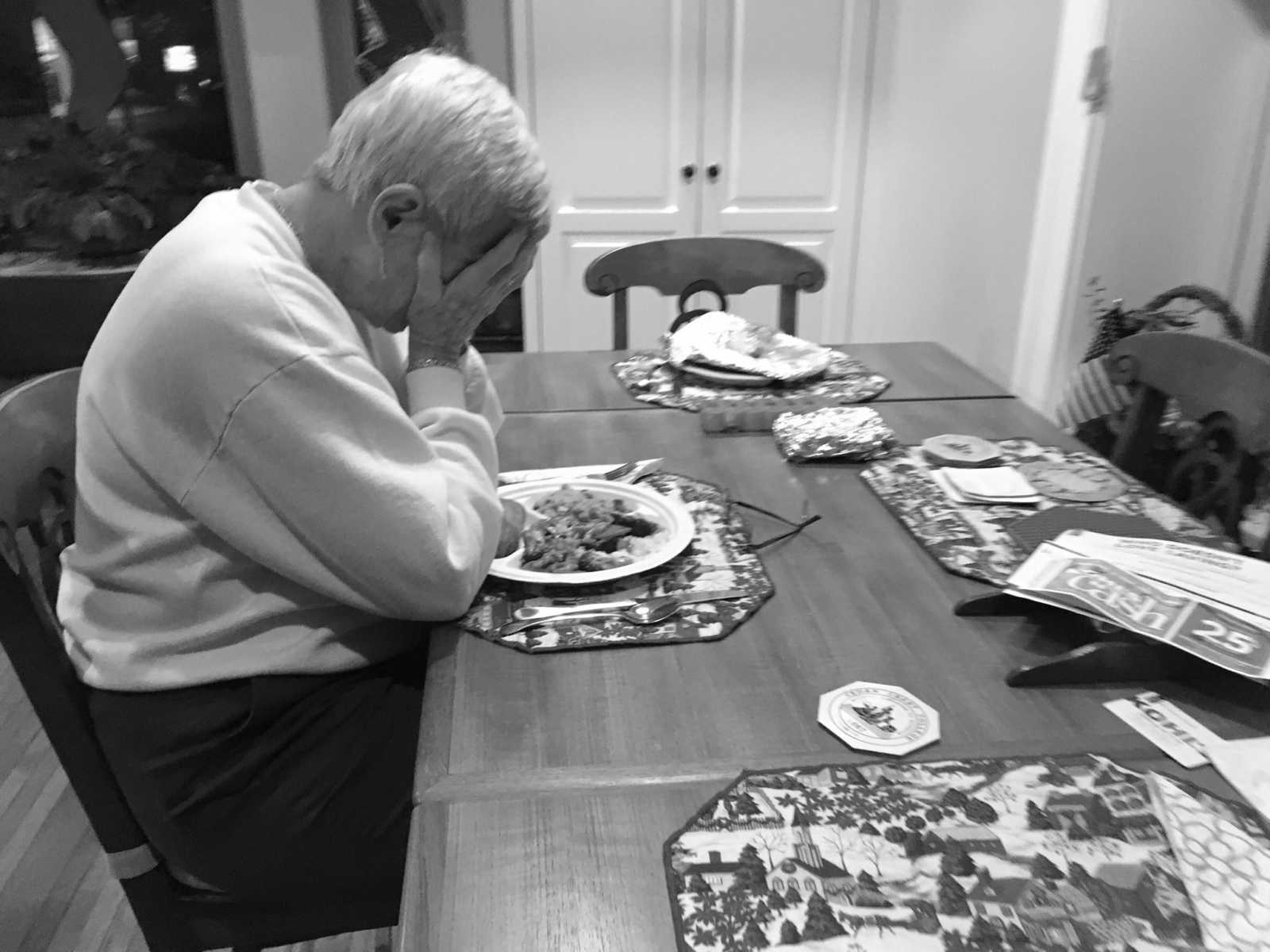 Woman with dementia sits alone at set table with head in her hands