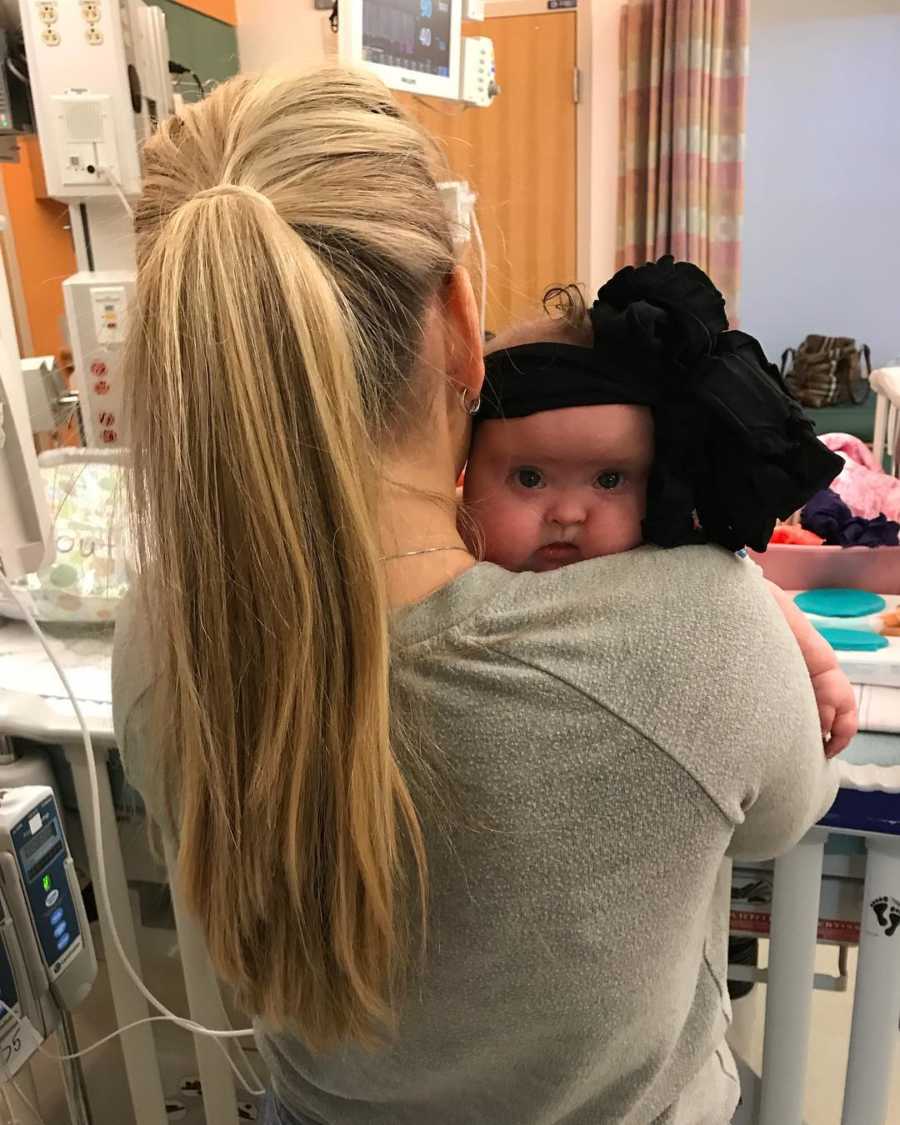 View of mother's back holding baby girl with black bow on head who would soon go to Children's hospital
