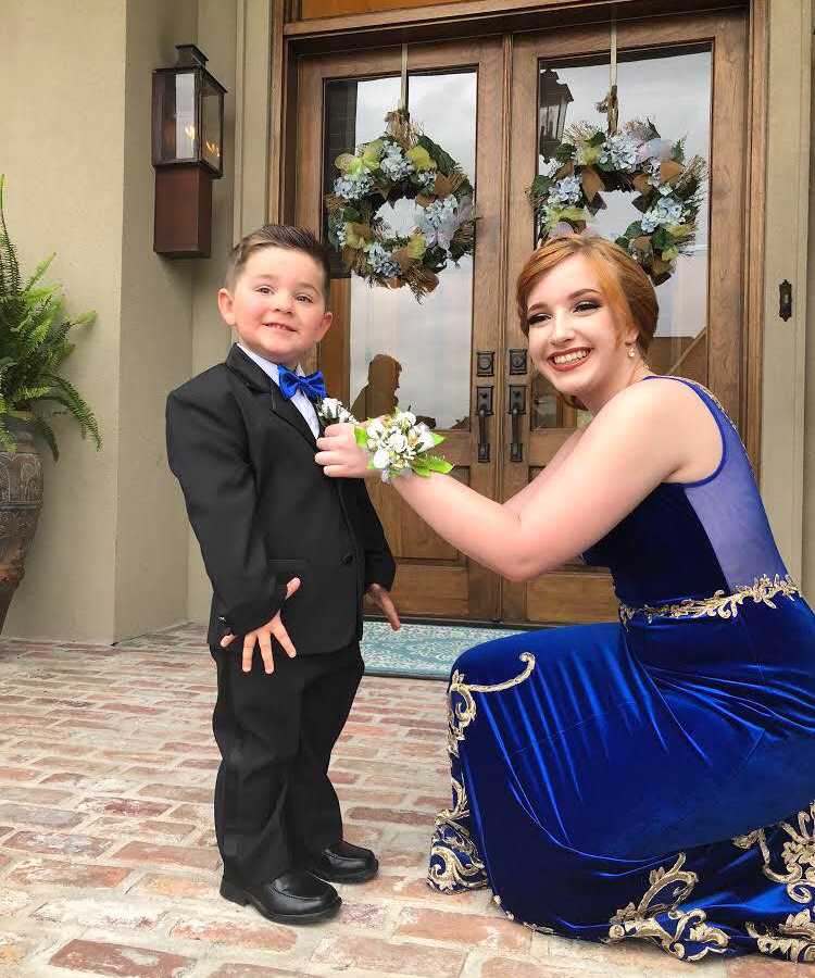 Girlfriend of marine crouches down to put boutonniere on marine's little brother who is a stand in prom date