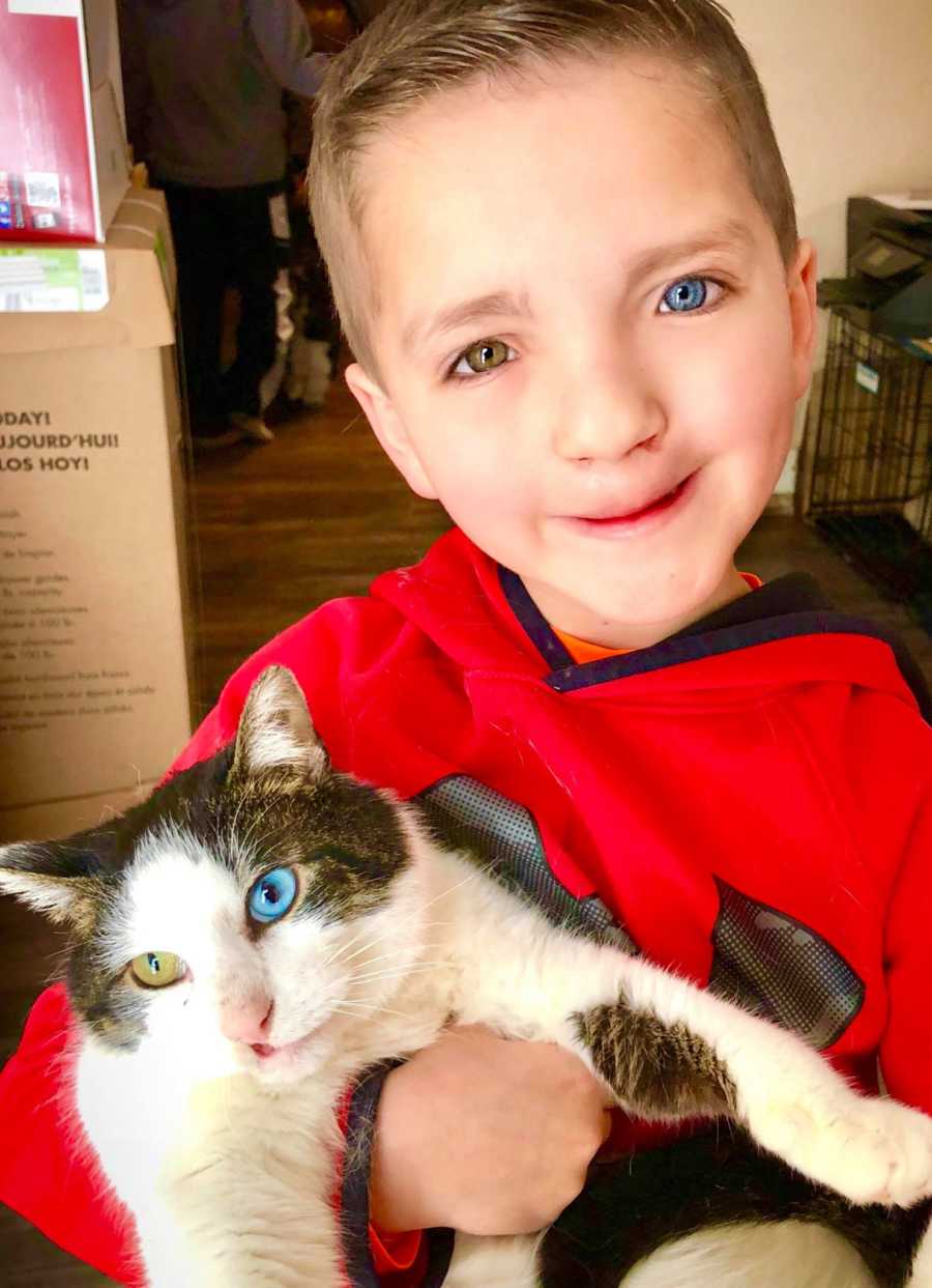 Little boy with two different colored eyes holds cat with same two different colored eyes