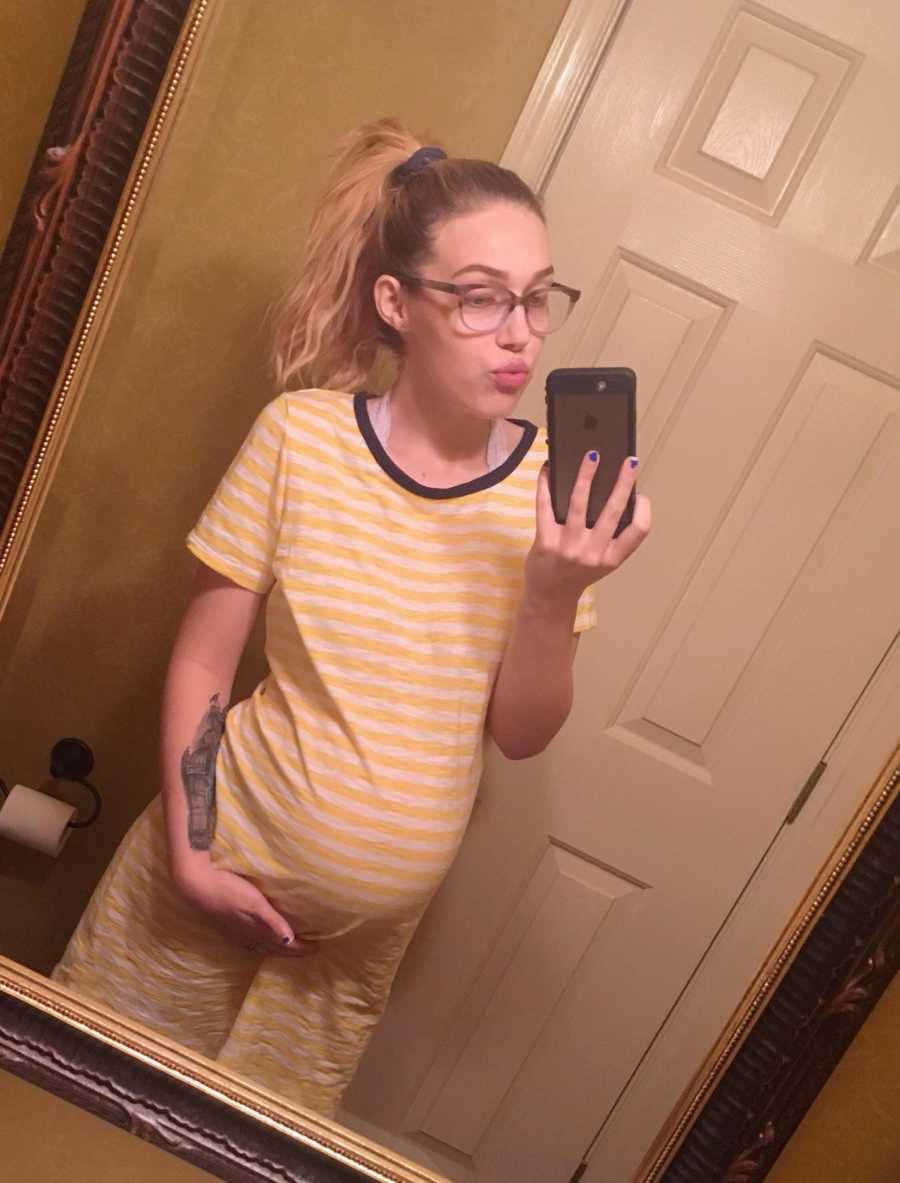 Pregnant woman holds bottom of stomach in mirror selfie