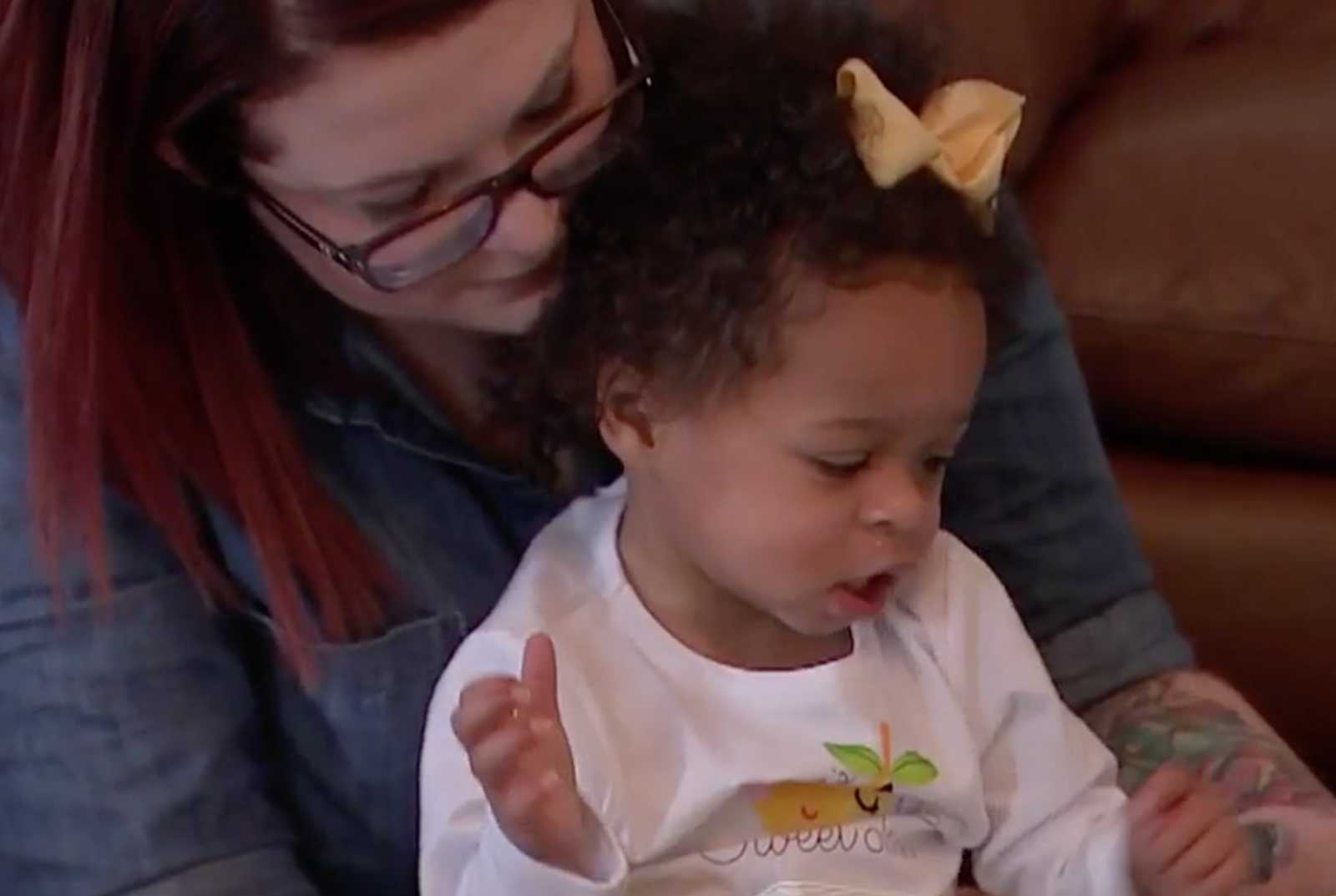 Close up of mother sitting with adopted toddler in her lap who was once abused