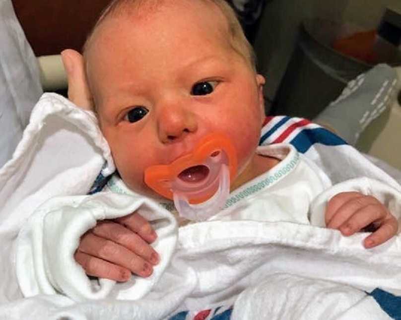 Newborn miracle baby lying in someones in arms in a blanket with orange pacifier in mouth