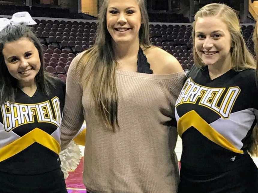Woman who didn't know she was pregnant stands with arms around two teenage cheerleaders