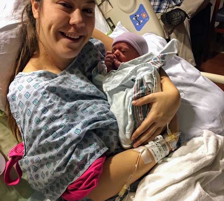 Woman who didn't know she was pregnant smiles in hospital bed holding swaddled newborn